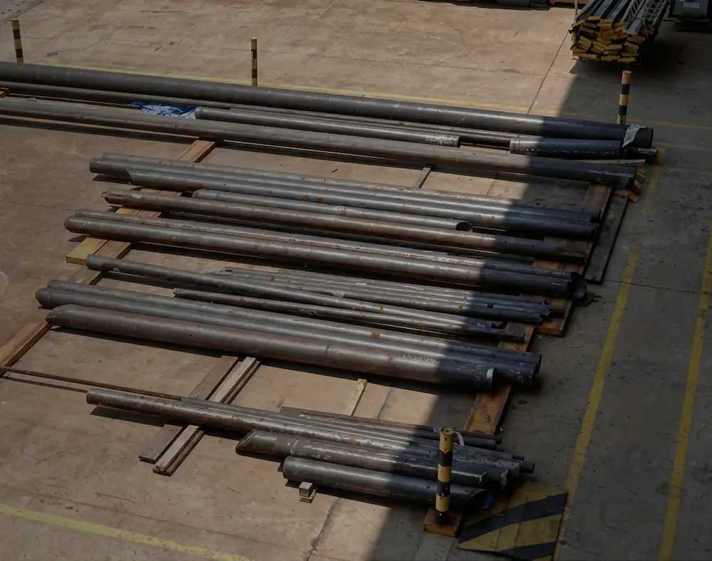 Stacks of long metal pipes arranged on wooden pallets in an outdoor industrial area.